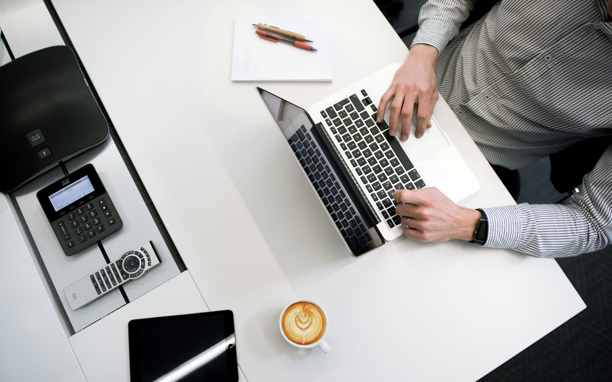 A person typing at a laptop on a white desk, seen from above