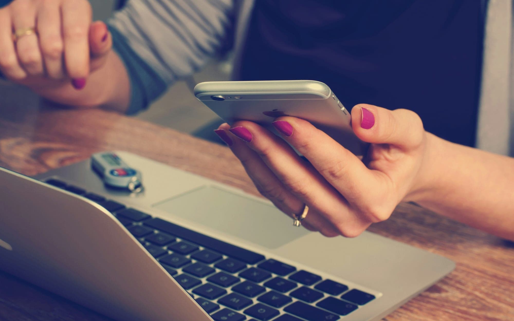 A person using a phone with one hand while working at a laptop